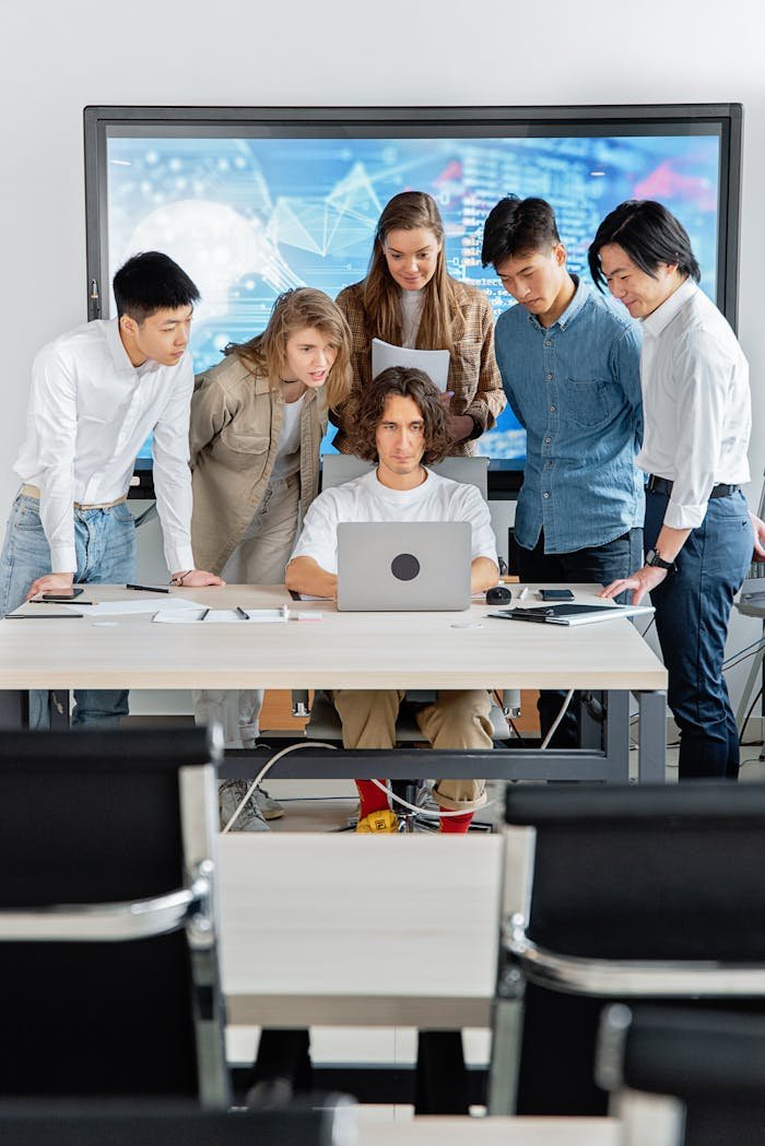 A diverse group of professionals engaged in teamwork around a laptop in a contemporary office setting.
